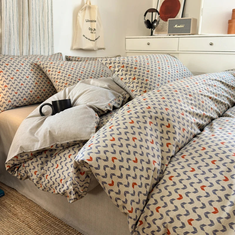 Patterned bedding on a bed in a room with a shelf and decor items.