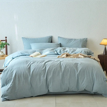 Light blue bedding set on a bed in a room with a lamp and plant.
