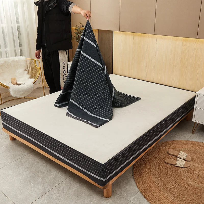 Person holding a striped blanket over a mattress in a bedroom setting.