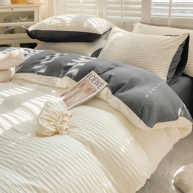 Gray and white bedding set on a bed with a LOEWE magazine.