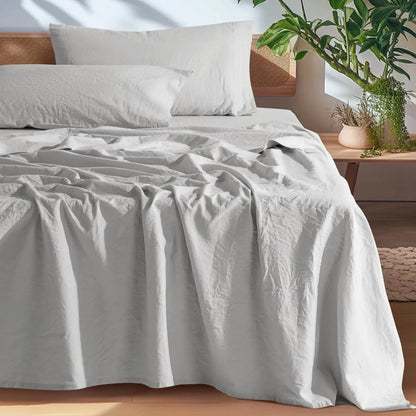 Gray bedding set on a bed with a wooden headboard and plants in the background.