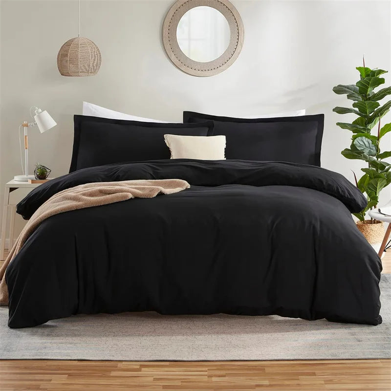 Black bedding set on a bed in a bedroom with a lamp and plant.
