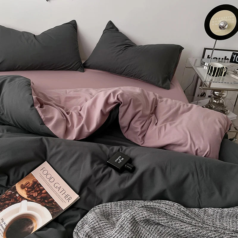 Bed with gray and pink bedding, a book, and a small clock on a nightstand.