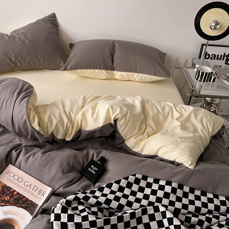 Bed with gray and beige bedding, checkered blanket, and a small table with decor items.