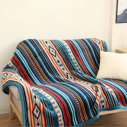 Colorful patterned blanket draped over a chair in a room with a white wall and a small table.