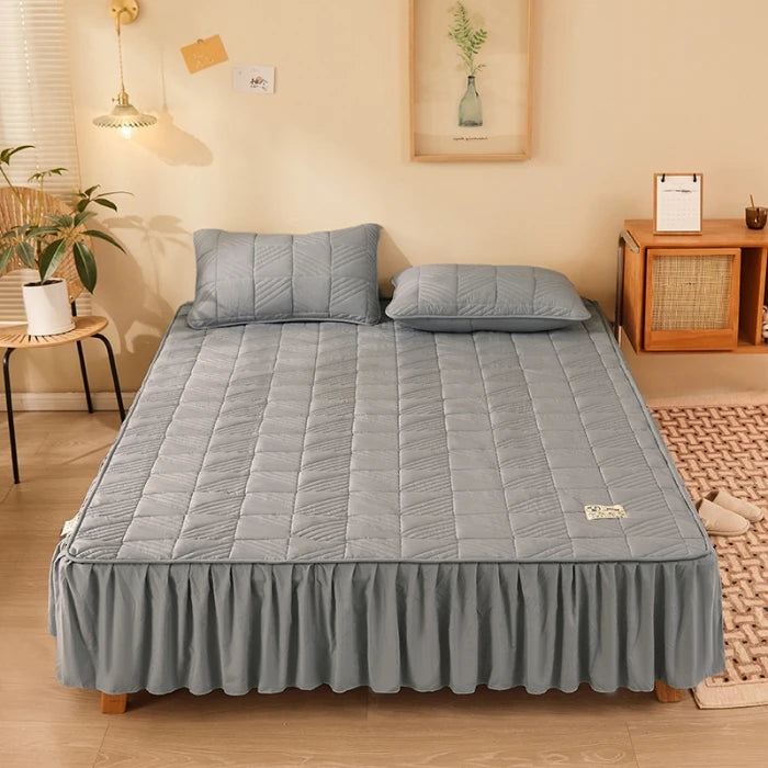 Gray quilted mattress cover on a bed in a bedroom setting.