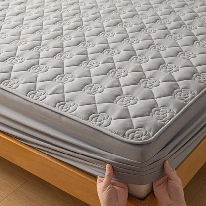 Person unfolding a gray quilted mattress cover on a wooden bed frame.