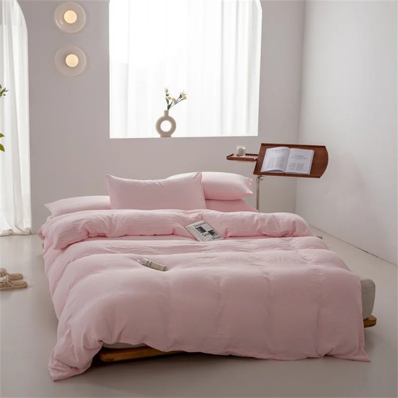 Pink bedding set on a bed in a minimalistic room with light gray walls and white curtains.