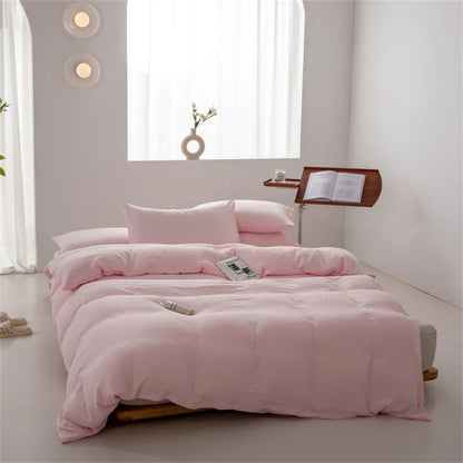 Pink bedding set on a bed in a minimalistic room with light gray walls and white curtains.