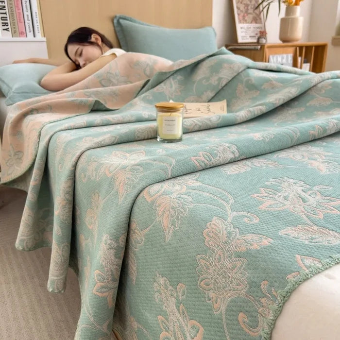 Woman lying on a bed with a floral-patterned comforter, candle, and books in the background.