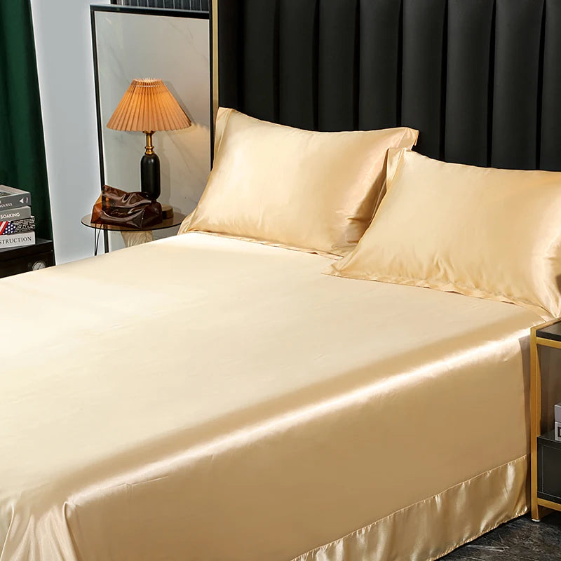 Beige satin bedding set on a bed with a lamp and books in the background.