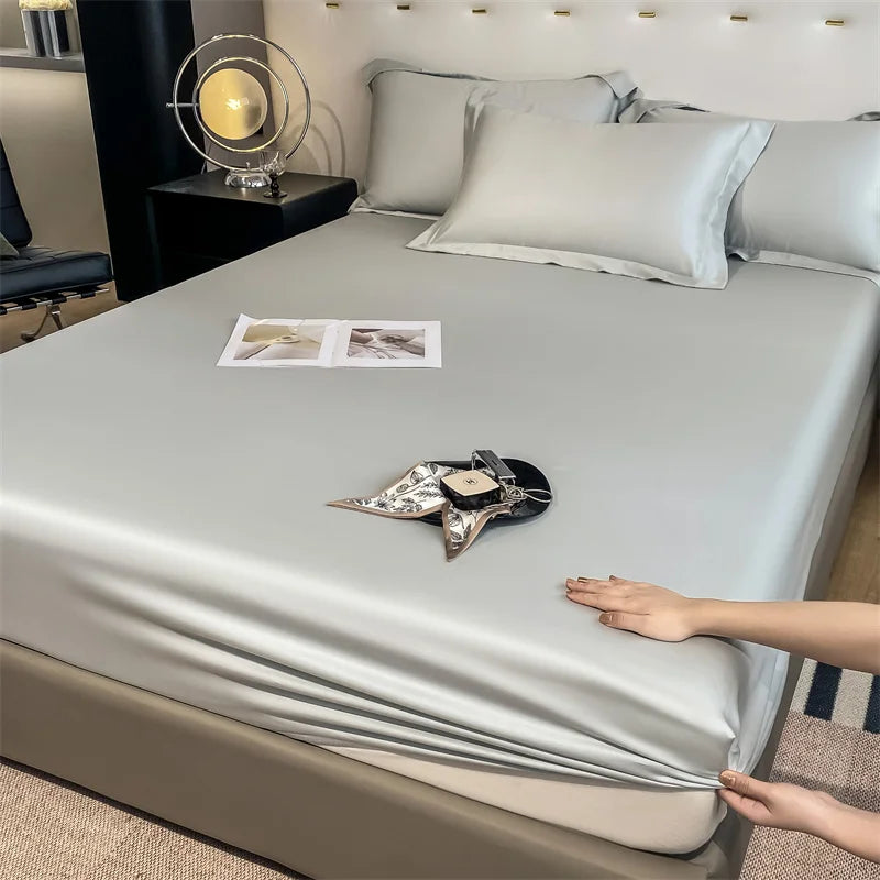 Person adjusting a silver satin sheet on a bed in a bedroom setting.