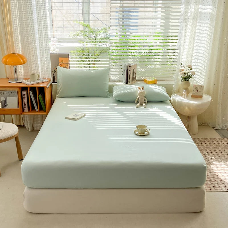 Bed with a light blue mattress cover in a bright room with curtains and a small table.