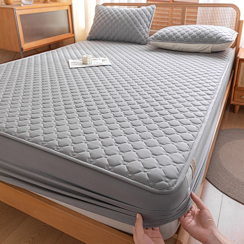 Gray quilted mattress cover being held by a person on a bed.