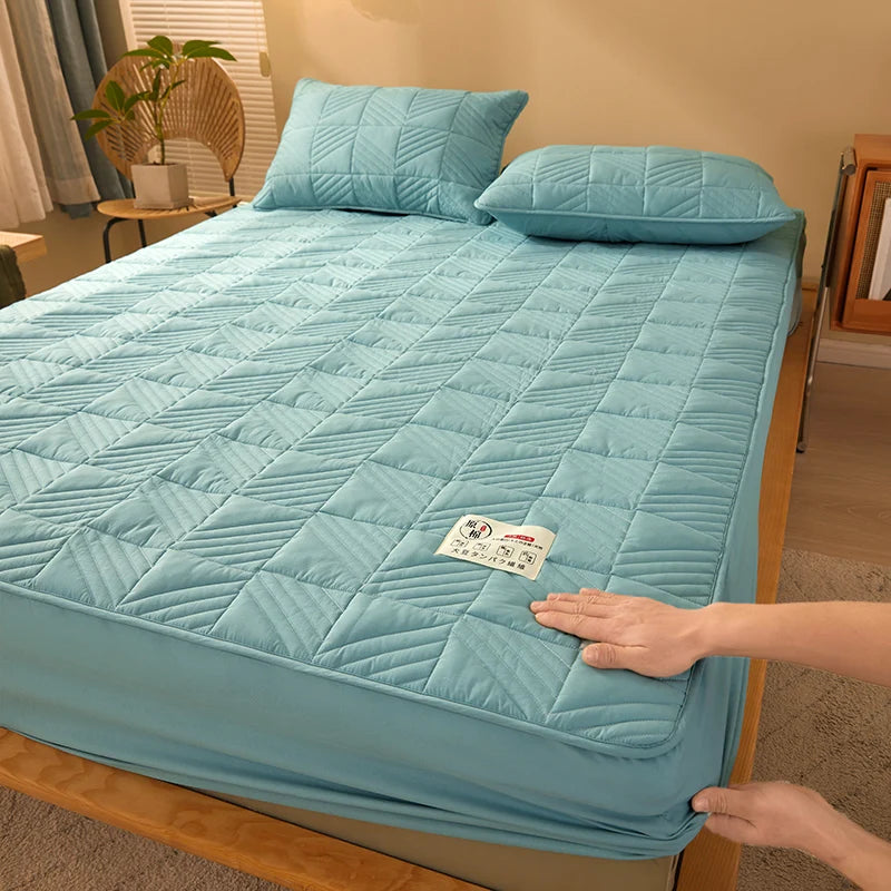 Person adjusting a blue quilted mattress cover on a bed in a bedroom.