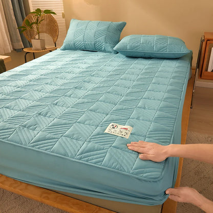 Person adjusting a blue quilted mattress cover on a bed in a bedroom.