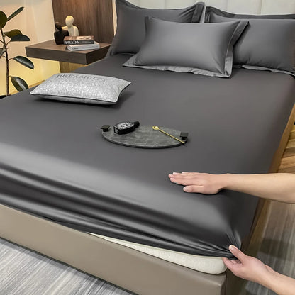Person adjusting gray fitted sheet on a bed with decorative pillows and a small table in the background.