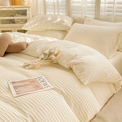 Neatly made bed with white bedding, pillows, and a teddy bear in a softly lit room.