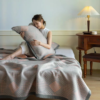 Woman sitting on a bed with a patterned quilt and pillow, in a cozy bedroom setting.