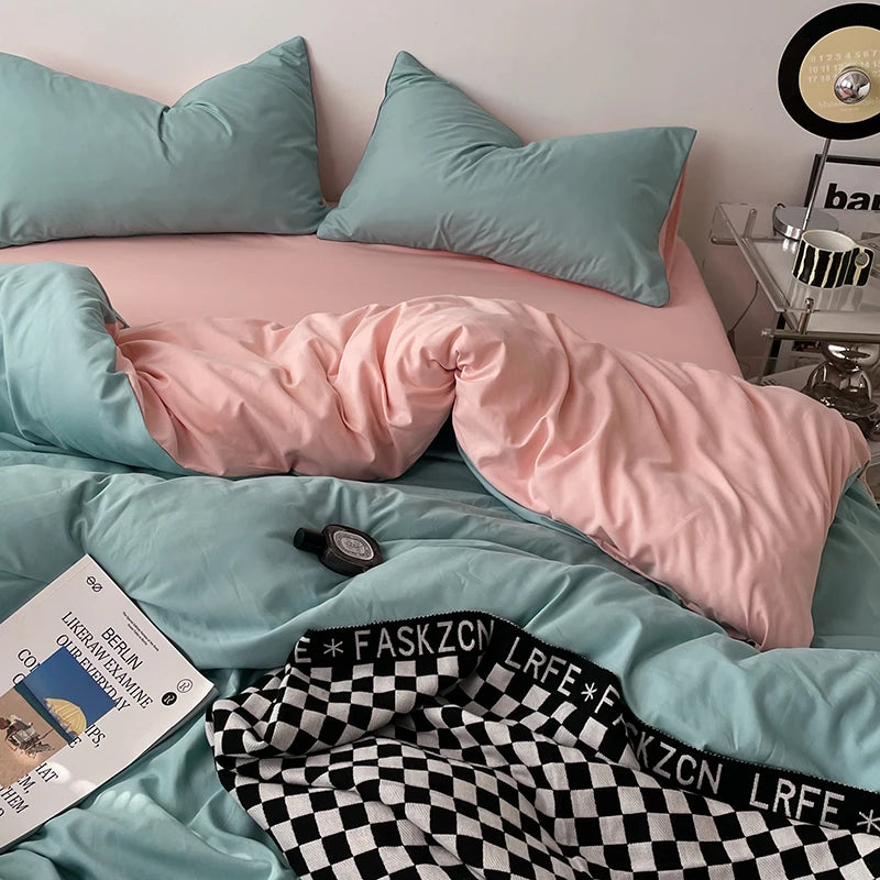 Teal and pink bedding set on a bed with a checkered blanket and book.