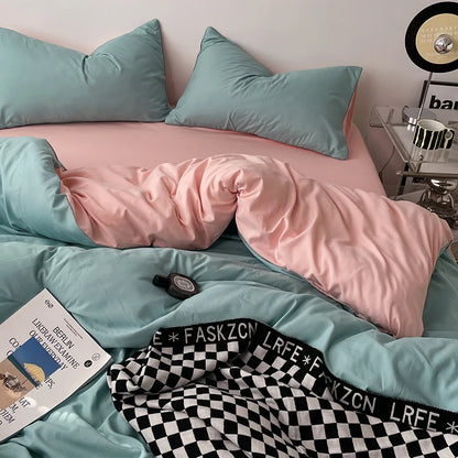 Teal and pink bedding set on a bed with a checkered blanket and book.