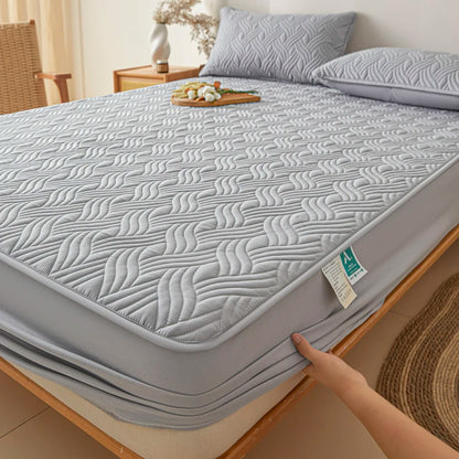 Gray quilted mattress cover on a bed with a hand touching it, in a bedroom setting.