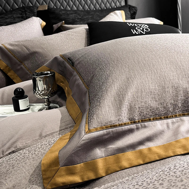 Gray and gold bedding set with a glass and bottle on a bed.