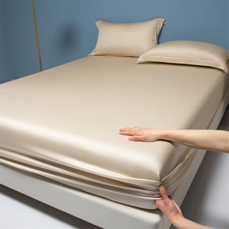 Beige satin sheet set on a bed with a hand demonstrating its smooth texture.