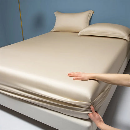 Beige satin sheet set on a bed with a hand demonstrating its smooth texture.