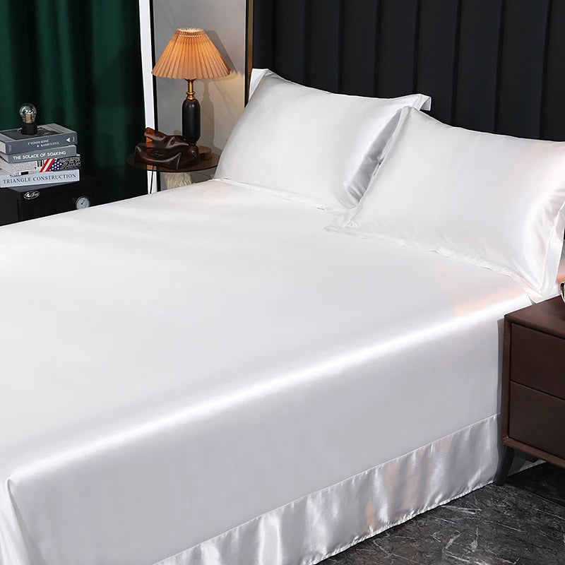 White satin sheet set on a bed with a lamp and books in the background.