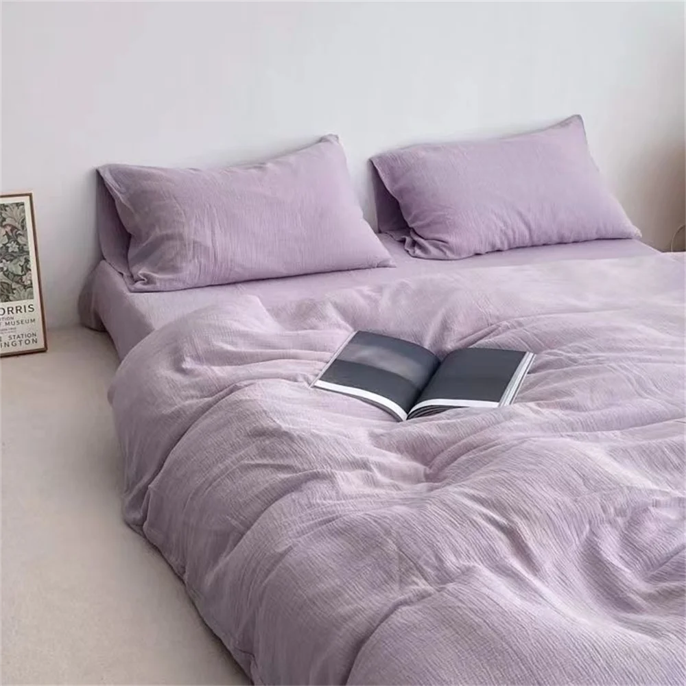 Purple bedding set with a book on a bed against a white wall.