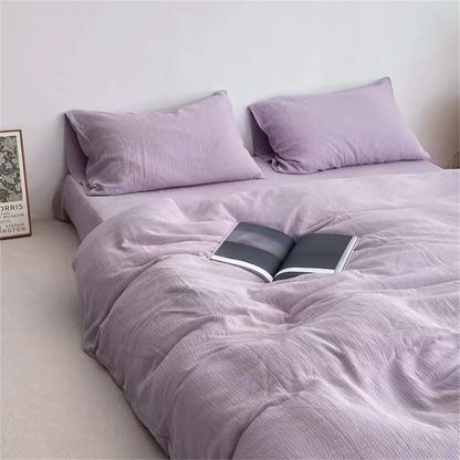 Purple bedding set with a book on a bed against a white wall.