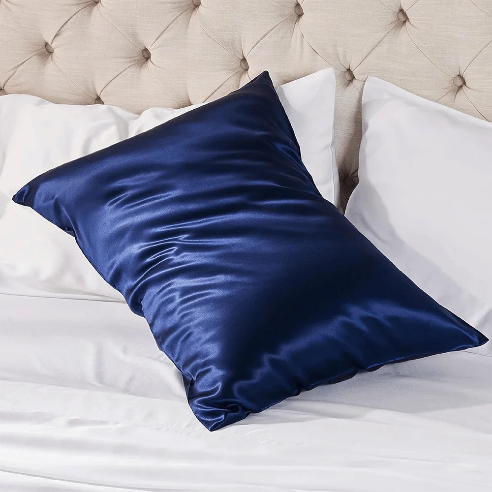 Blue satin pillow on a bed with white pillows and a tufted headboard.