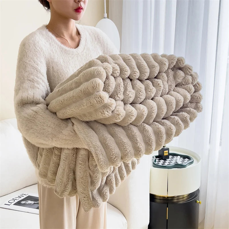 Person holding a large beige knitted blanket in a room with a white curtain and a small table.