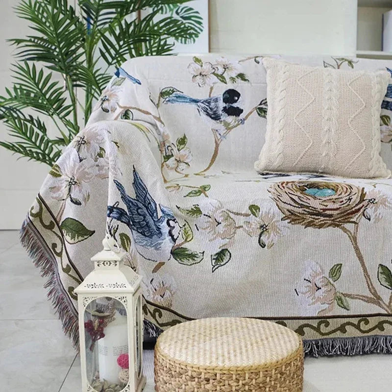 Decorative sofa with floral and bird patterned cover, lantern, and woven stool in a room.