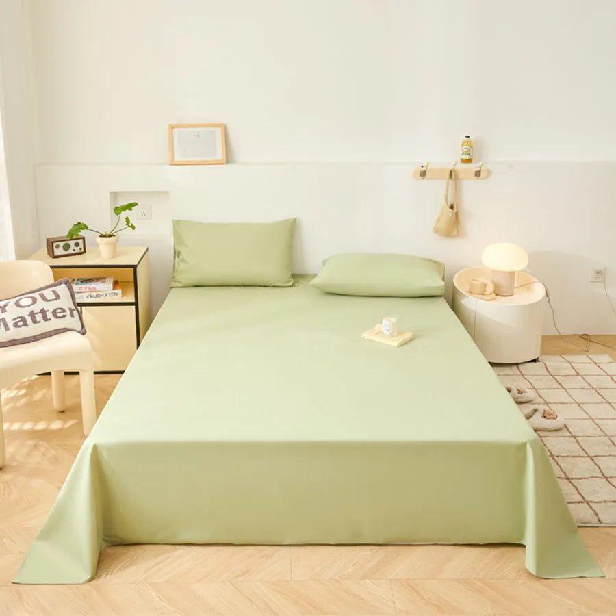 Bed with green bedding in a room with a chair, table, and decor items.