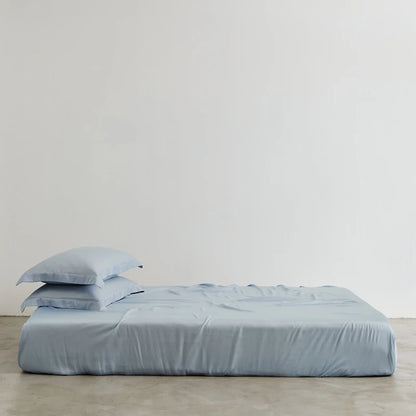 Light blue bed sheets and pillowcases on a bed against a plain background