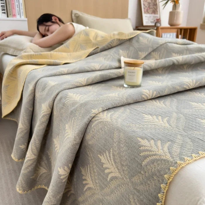 Person sleeping under a patterned blanket with a candle on a nightstand.