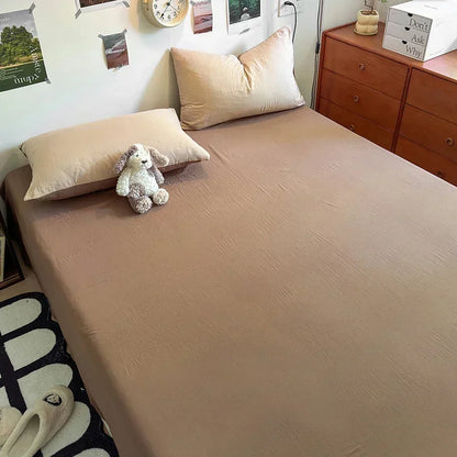 Bed with beige sheets and pillows, teddy bear, and wooden dresser in a bedroom.