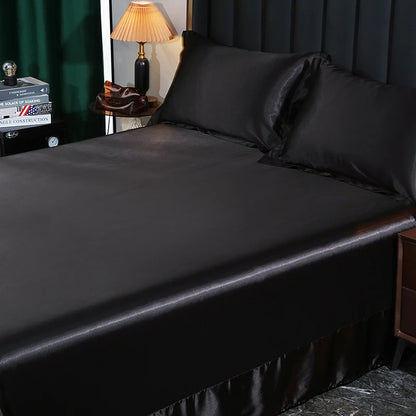 Black satin sheet set on a bed with a lamp and books in the background.
