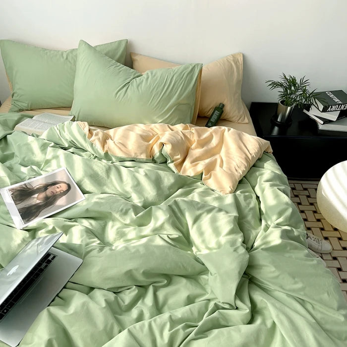 Bed with light green bedding and pillows, nightstand with books and plant.