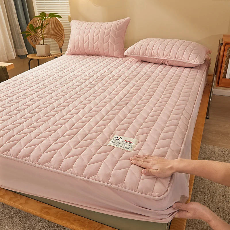 Person adjusting a pink quilted mattress cover on a bed in a bedroom.