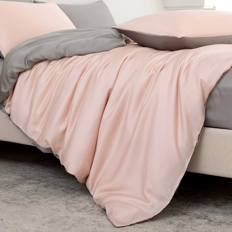 Pink blanket draped over a bed with gray pillows.
