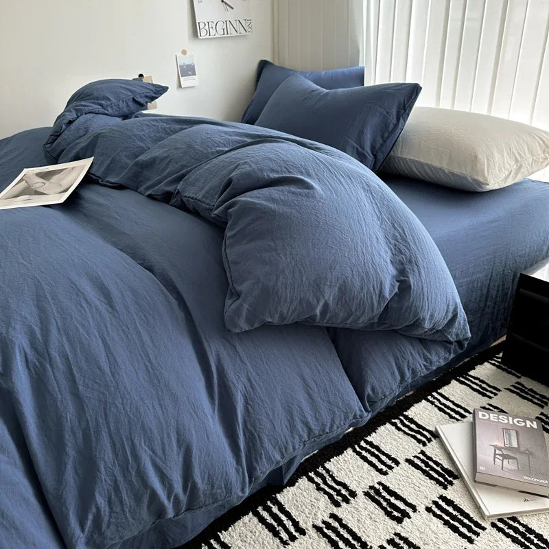 Blue bedding set on a bed with a white wall and books in the background
