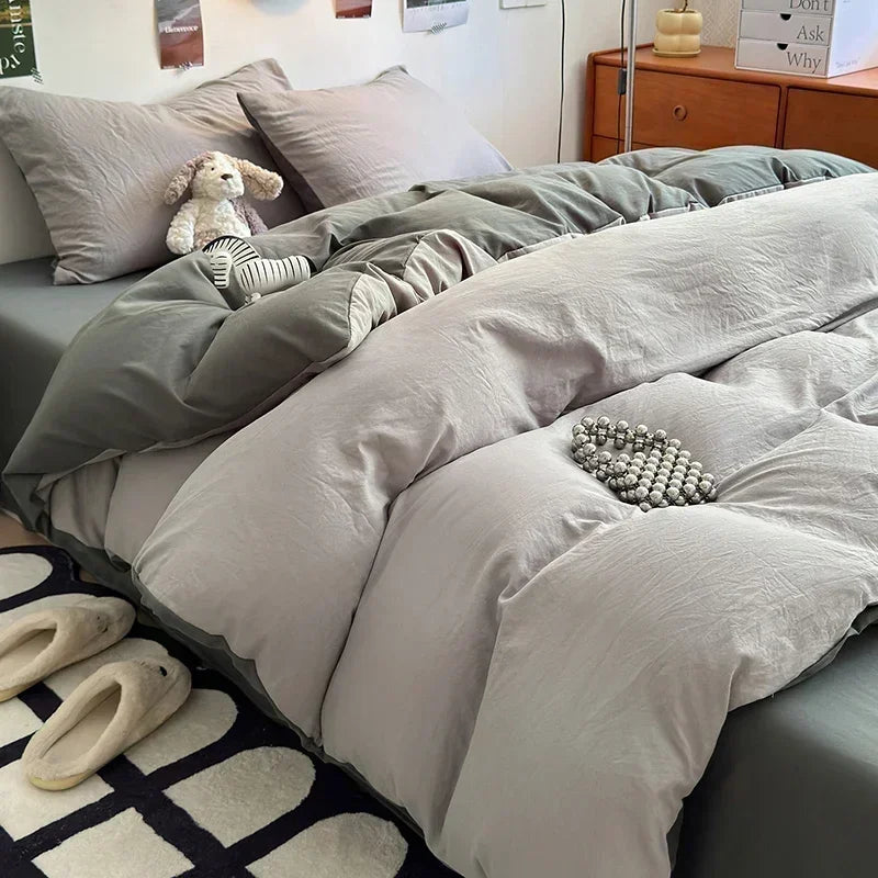 Gray bedding set on a bed with pillows and slippers in a bedroom.
