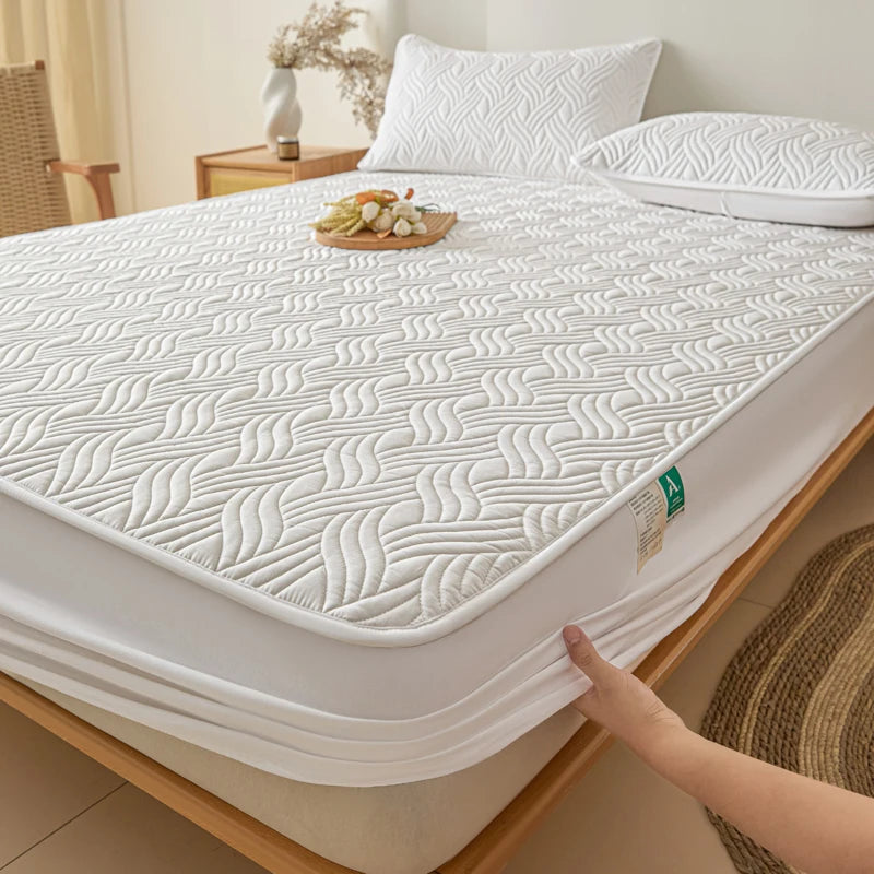 White mattress cover on a bed with a hand holding it, in a room setting.