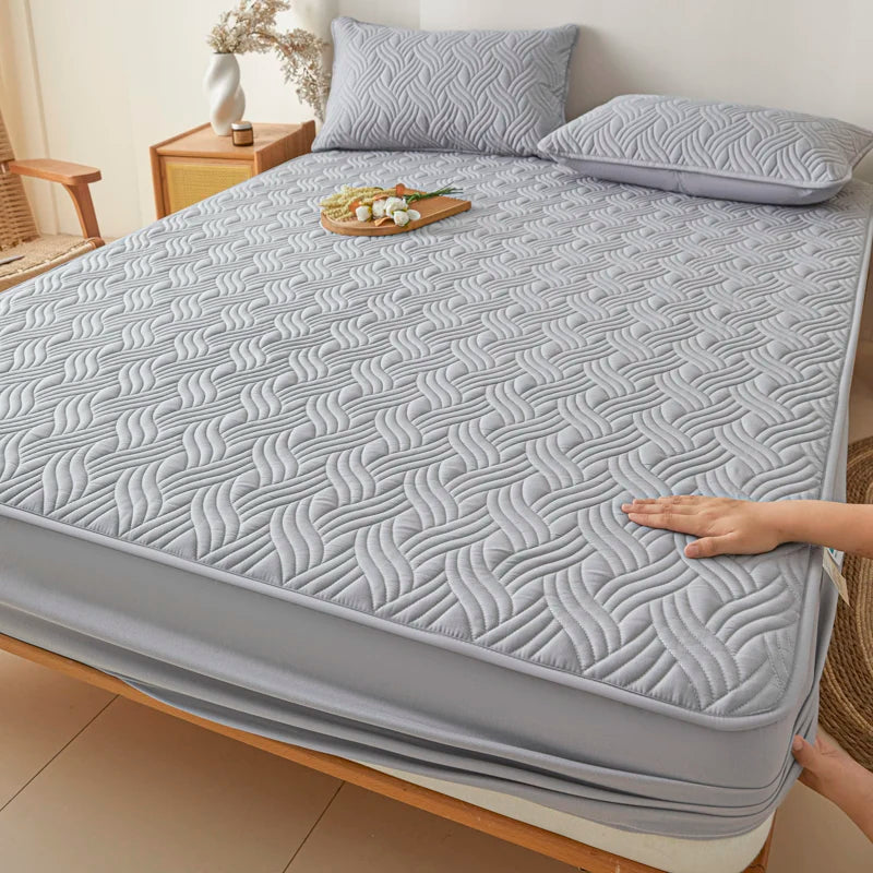 Gray quilted mattress cover on a bed with a hand touching it, in a bedroom setting.