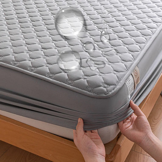 Gray mattress cover being adjusted on a bed with water droplets showing its waterproof feature.