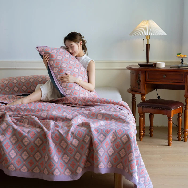 Woman sitting on a bed with pink and white patterned bedding in a room with wooden furniture and a lamp.