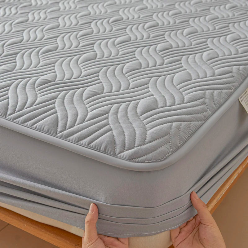 Gray mattress cover with wavy pattern held by hands on a wooden surface
